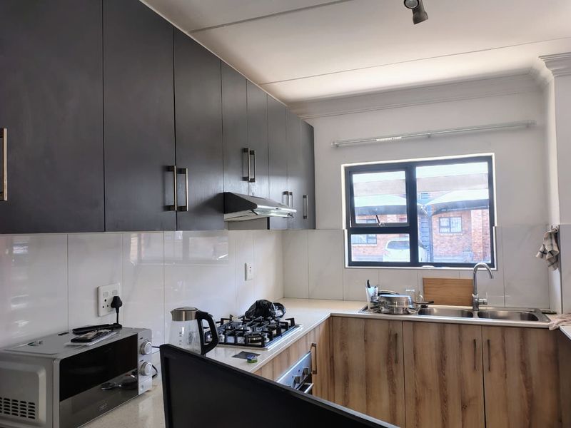 Modern kitchen featuring dark upper cabinetry, wood-finish lower cabinets, stone countertops, a gas hob, and a double sink with a tiled splashback.