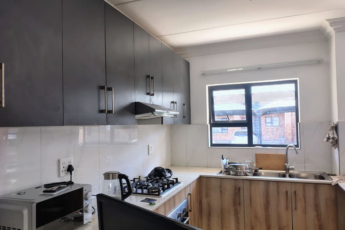 Modern kitchen featuring dark upper cabinetry, wood-finish lower cabinets, stone countertops, a gas hob, and a double sink with a tiled splashback.