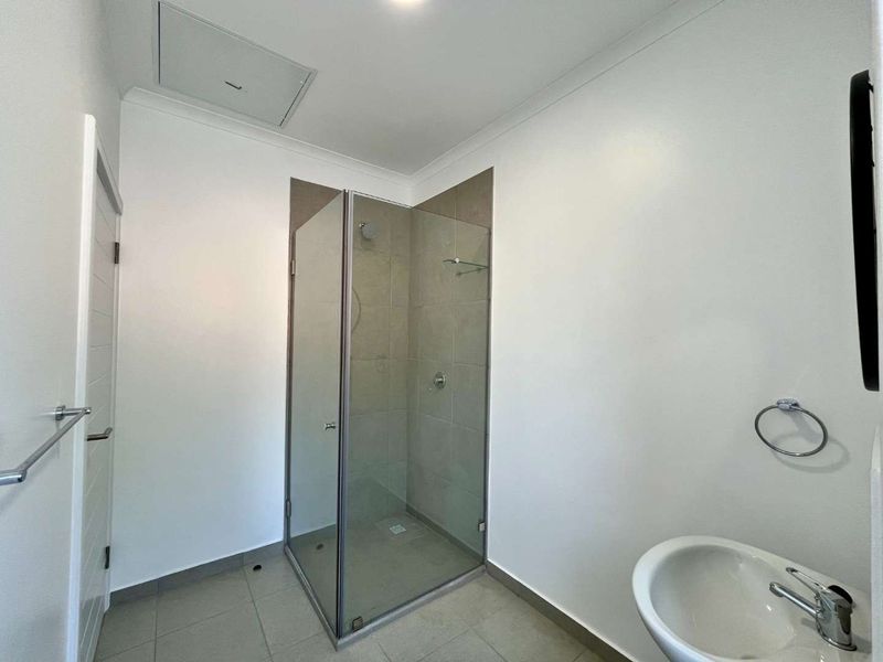 A clean, modern bathroom featuring a glass-enclosed shower with tiled walls, a pedestal basin with chrome fixtures, and neutral floor tiling.