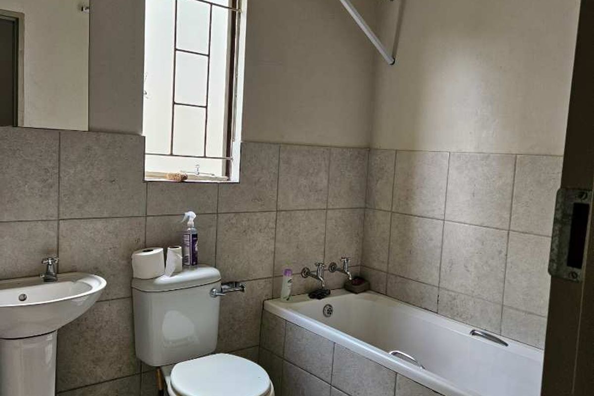 A functional bathroom featuring a pedestal basin, standard toilet, and a bathtub with tiled surround, complemented by a wall-mounted drying rack.