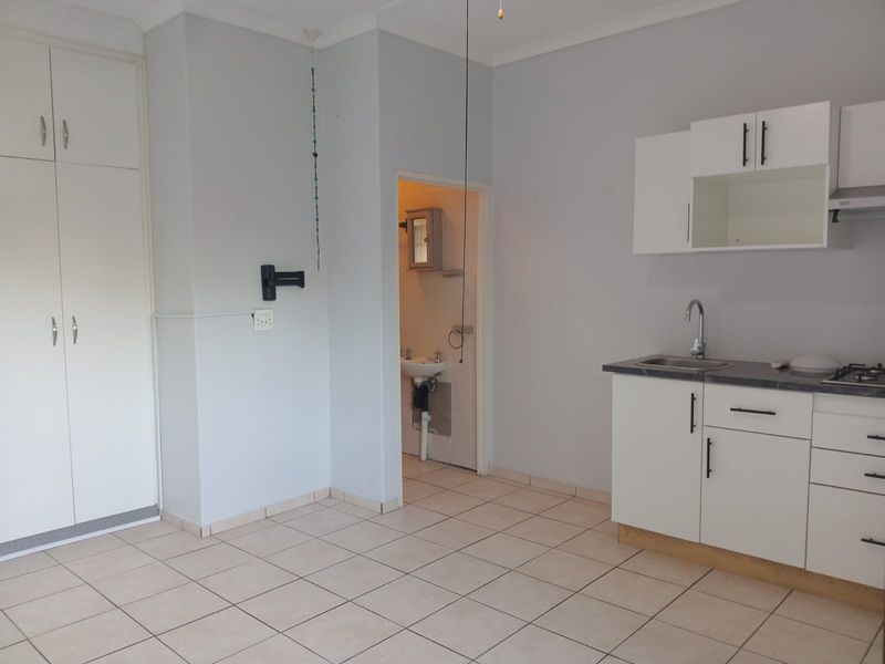 Open plan living area featuring a compact kitchenette with built-in cabinetry, tiled flooring, and direct access to an adjoining bathroom.