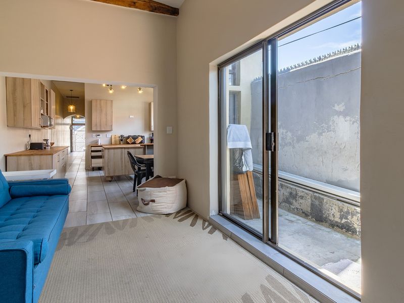 Open-plan living and kitchen area featuring tiled floors, exposed ceiling beams, and large sliding doors opening to a private rear courtyard.
