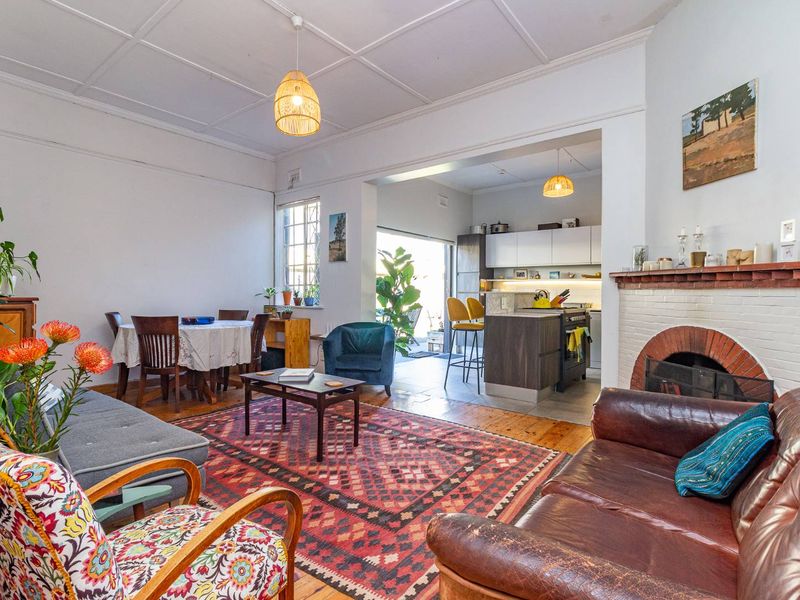 Open plan living and dining area featuring a brick fireplace, timber flooring, and direct access to the kitchen and outdoor space.