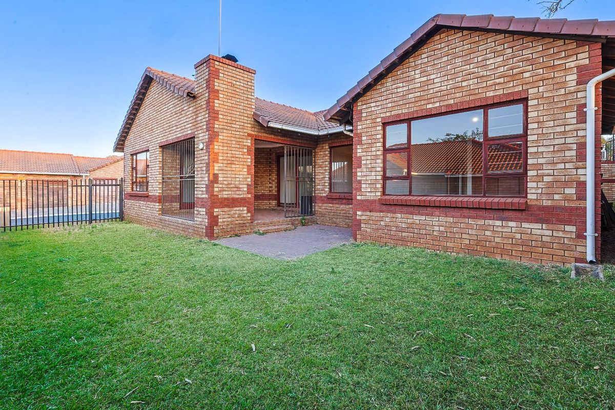 Rear view of a face-brick house featuring a paved patio area, secure metal fencing, and a well-maintained lawn.