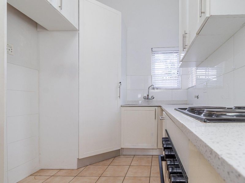 A clean and functional kitchen featuring white cabinetry, stone countertops, a built-in hob, and tiled flooring with ample storage space.