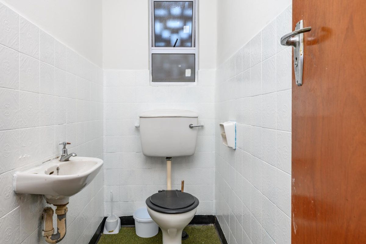 A compact guest bathroom featuring a wall-mounted basin and a standard toilet, finished with white wall tiles and a functional window.