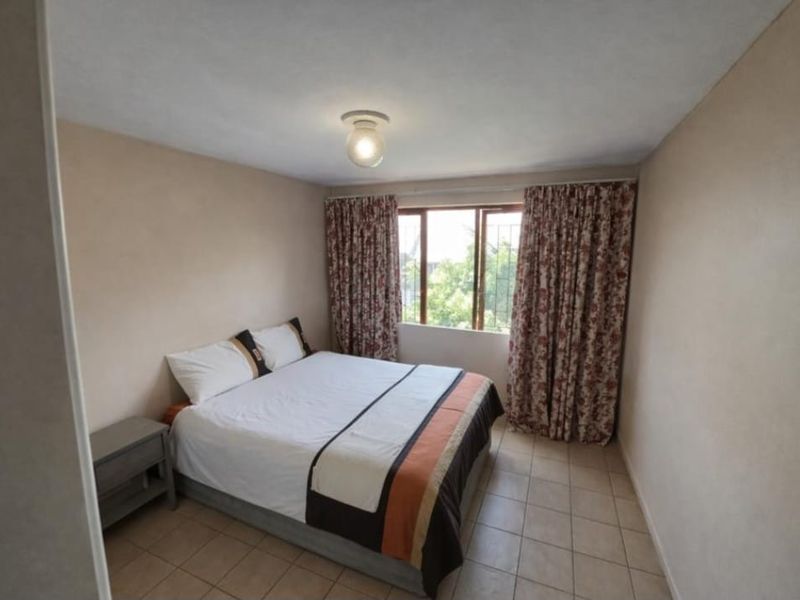 A functional bedroom featuring tiled flooring, a central ceiling light, and a window fitted with security bars.