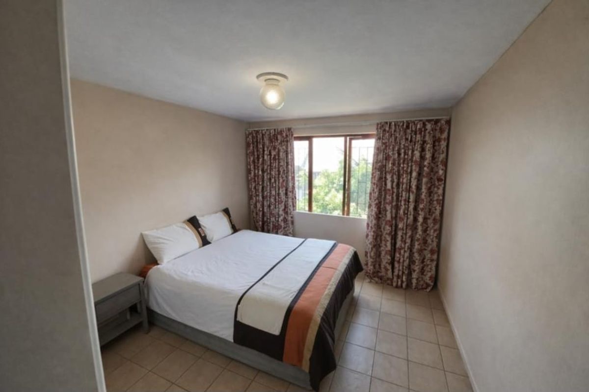 A functional bedroom featuring tiled flooring, a central ceiling light, and a window fitted with security bars.