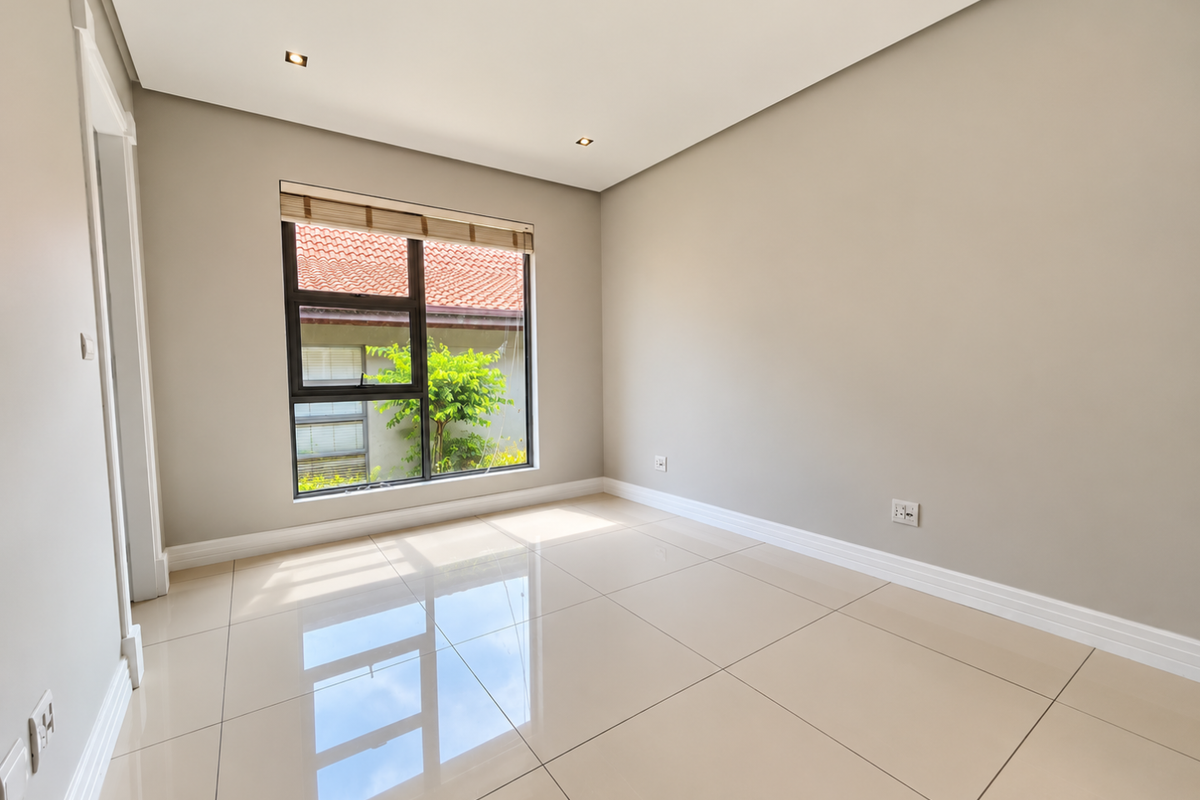 A bright, empty bedroom featuring neutral walls, polished tiled flooring, recessed downlights, and a large window with views of the exterior.