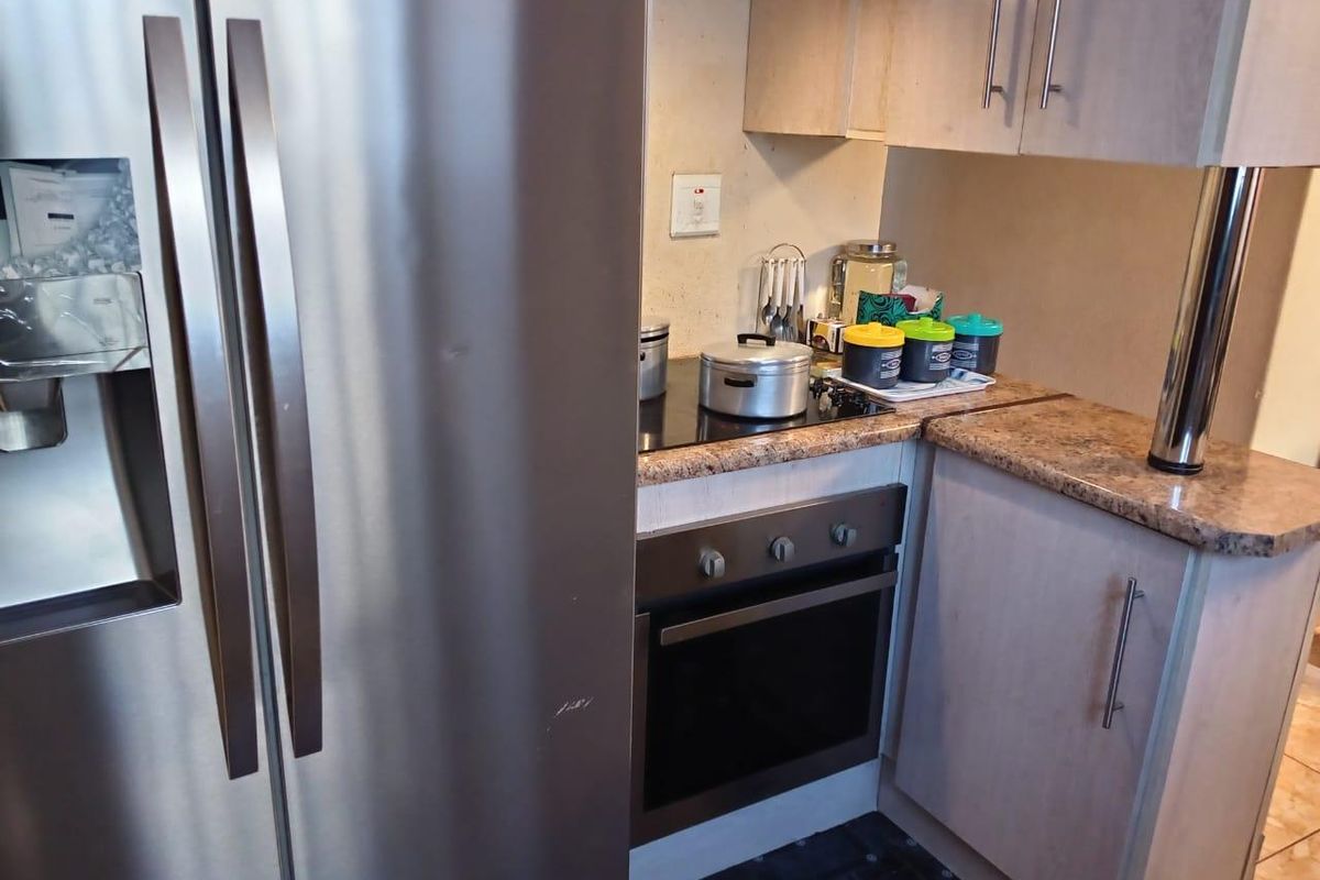 Compact kitchen area featuring built-in oven, electric hob, extractor fan, and laminate countertops with light-toned cabinetry.