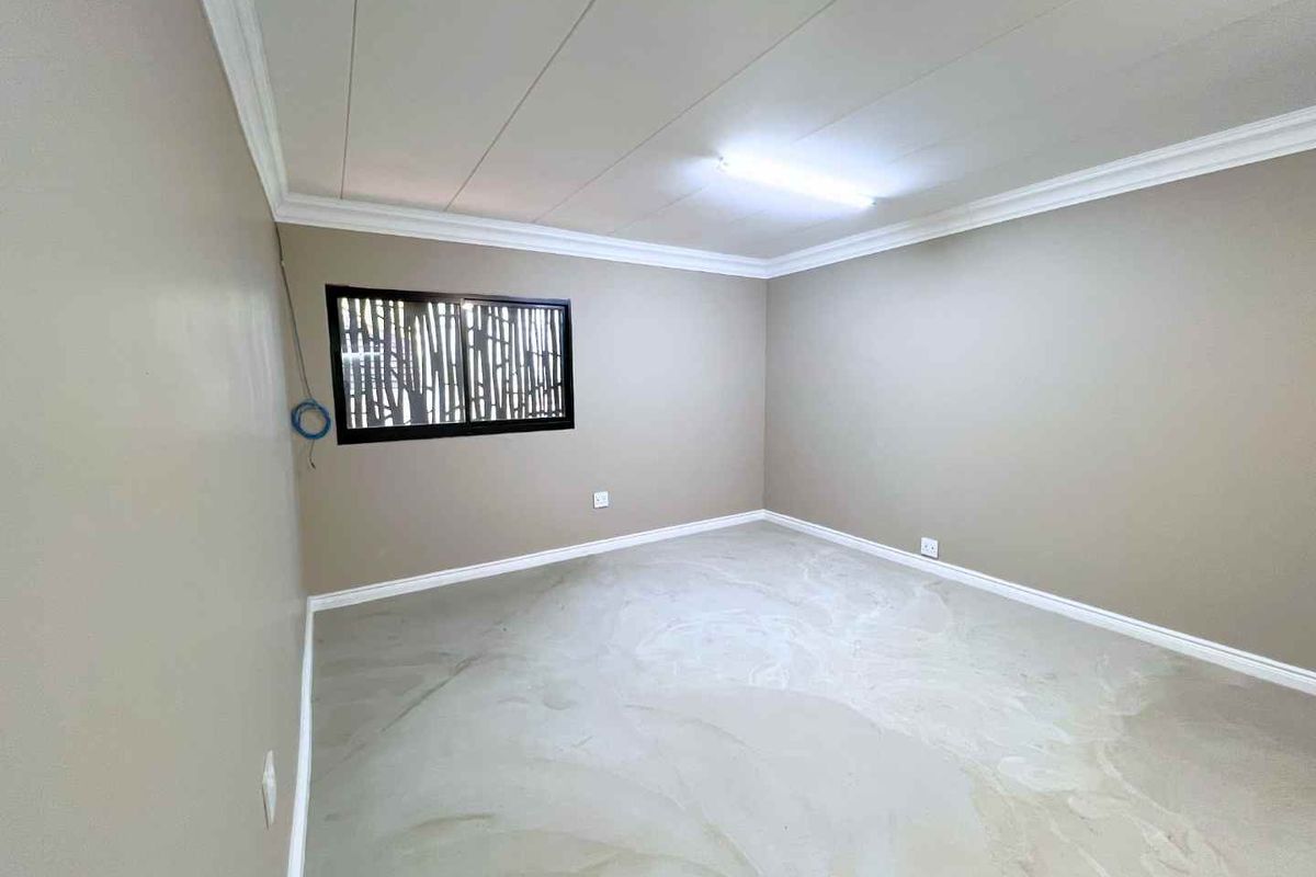 An empty bedroom featuring neutral wall paint, crown molding, and a security screen window with a polished concrete floor finish.