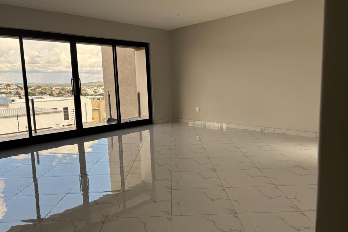 A bright, modern living area featuring large sliding glass doors, polished marble-look floor tiles, and neutral wall finishes with access to an outdoor balcony.
