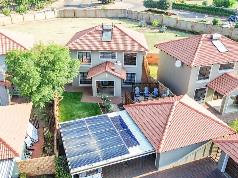 Aerial view of a residential property featuring a tiled roof, solar panels, solar geyser, and a paved driveway within a secure estate.