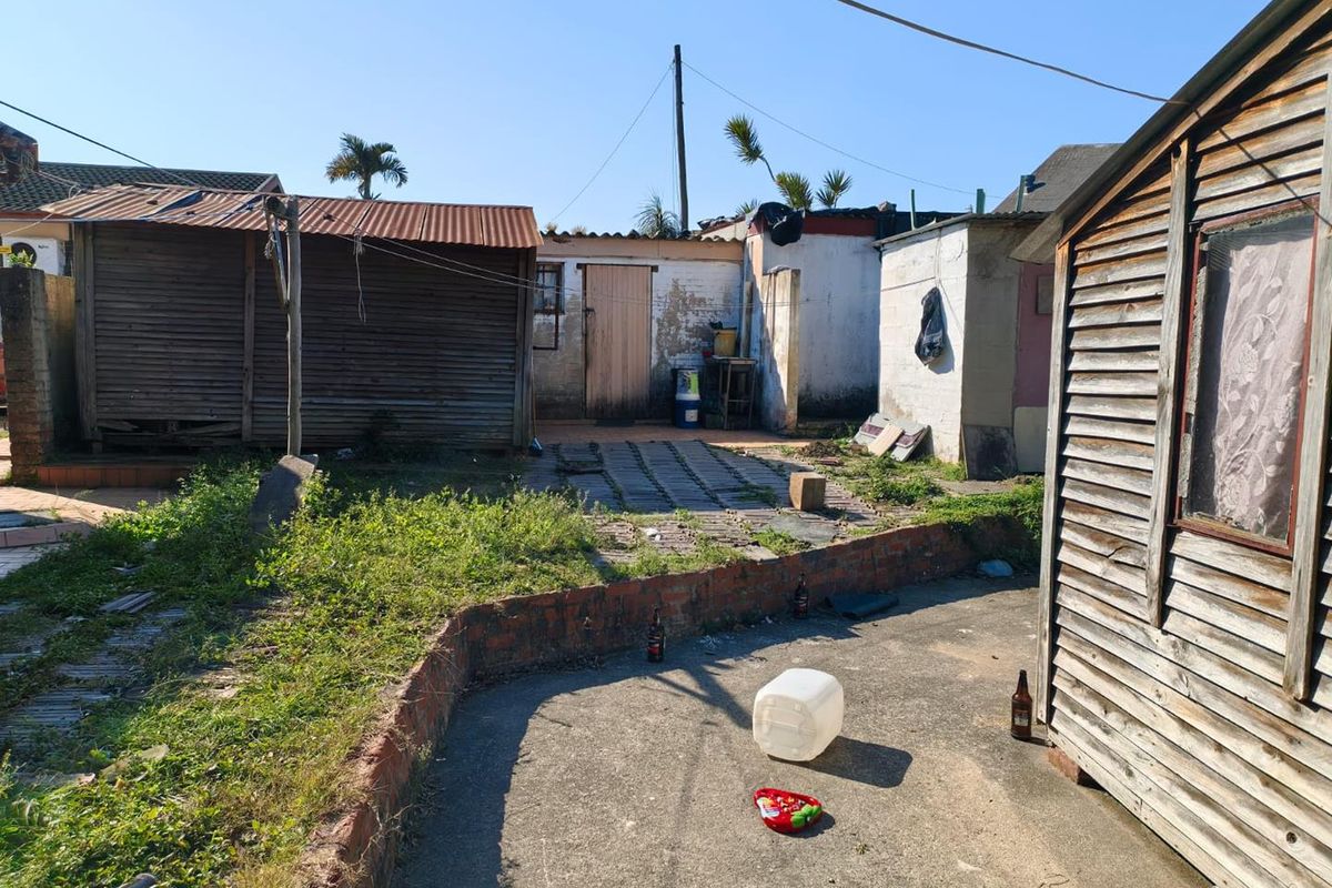 Rear yard area featuring weathered timber structures, brick retaining walls, and concrete paving, requiring significant maintenance and landscaping improvements.