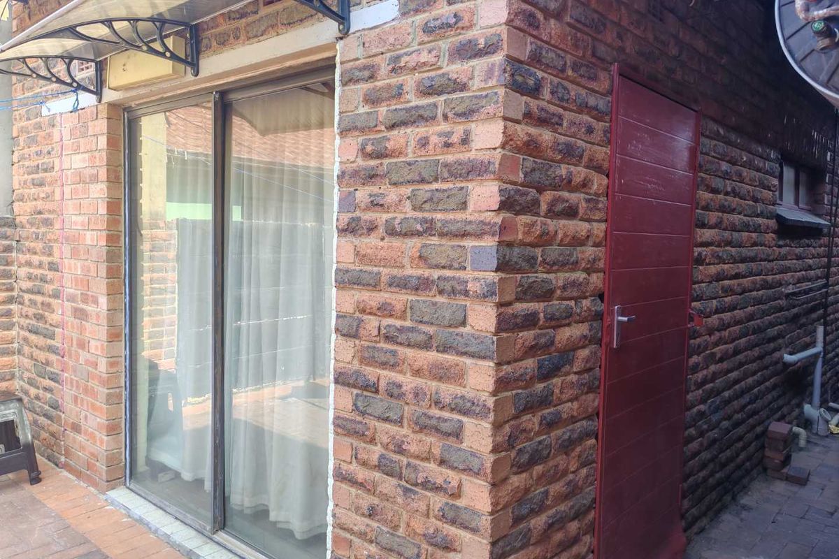 Exterior view of the rear facade featuring face brick walls, a sliding glass door with an awning, and a side access door.