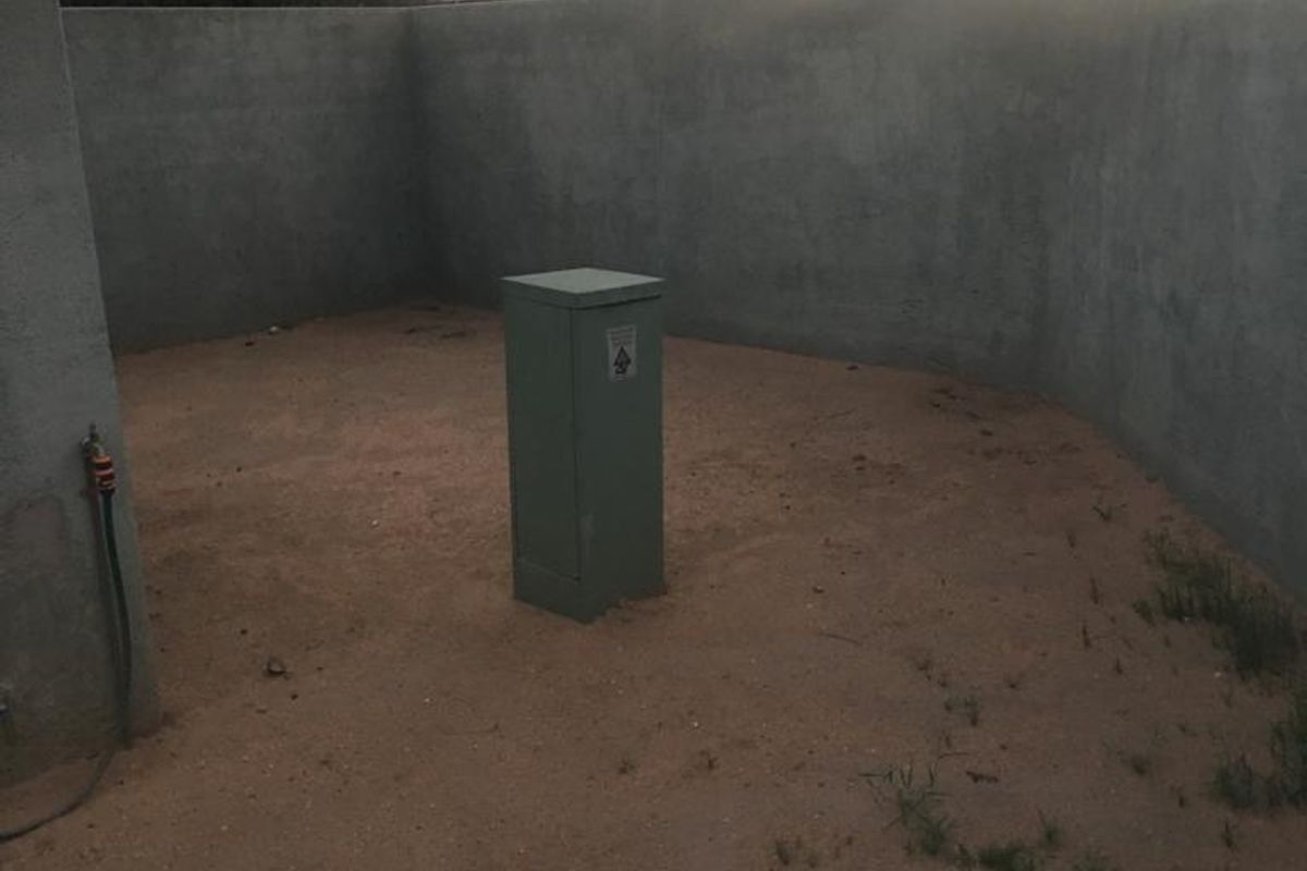 A private rear courtyard area featuring plastered boundary walls, an external water tap, and an electrical utility box, currently with an unfinished ground surface.
