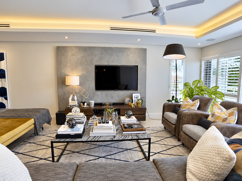 A modern, well-appointed living room featuring a feature wall, recessed ceiling lighting, ducted air conditioning, and plantation shutters opening to an outdoor area.