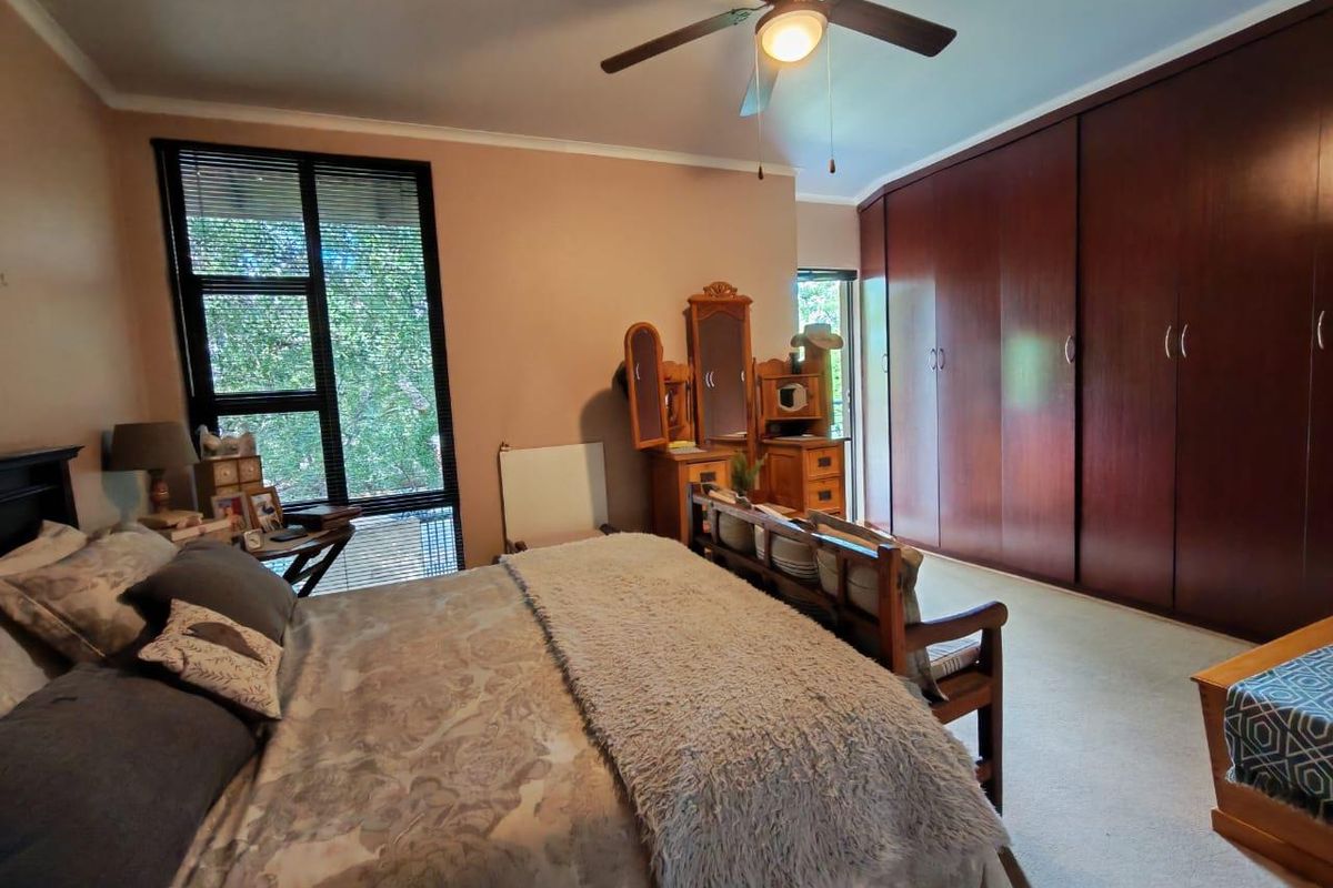 Spacious bedroom featuring large floor-to-ceiling built-in wooden wardrobes, a ceiling fan, and large windows providing natural light.