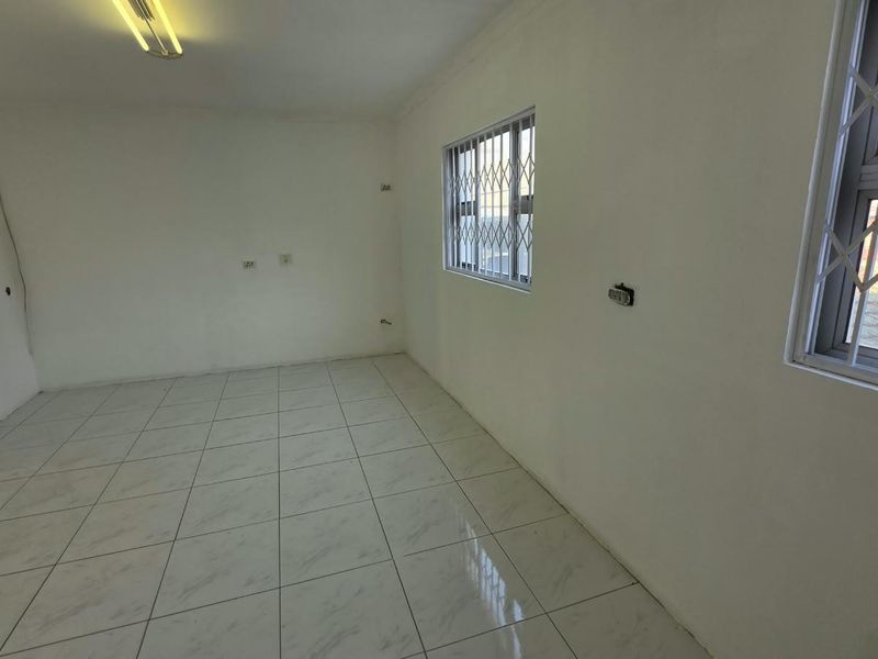 A vacant office space featuring tiled flooring, security bars on windows, and basic electrical infrastructure, ready for customization.