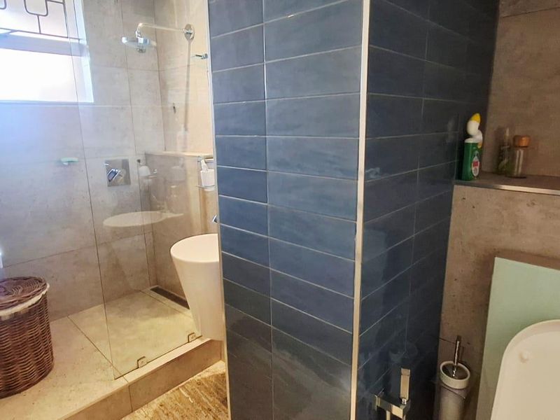 Modern bathroom featuring a glass-enclosed shower, blue subway tile accents, and neutral floor tiling.