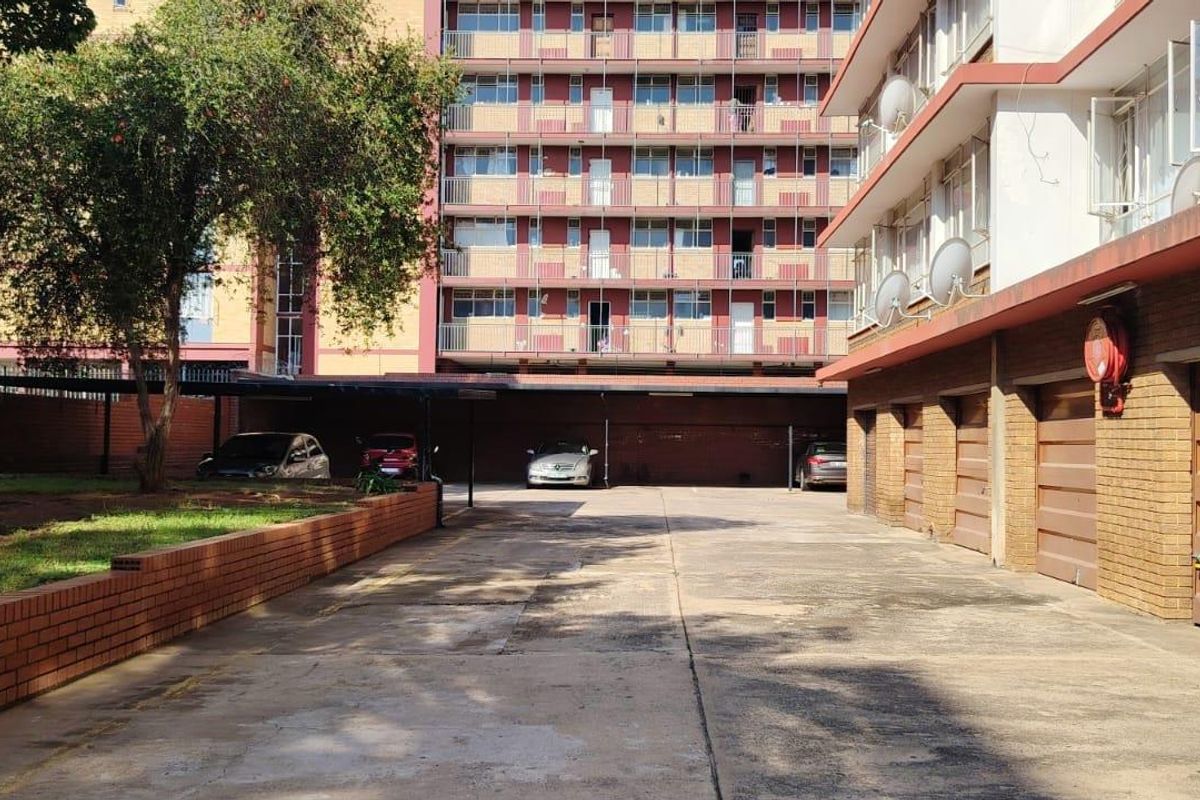 Exterior view of the apartment complex showing a concrete driveway, covered parking area, and row of garage doors.