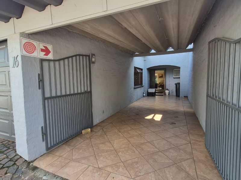 A covered driveway or garage entrance featuring tiled flooring, metal security gates, and direct access to the main dwelling.
