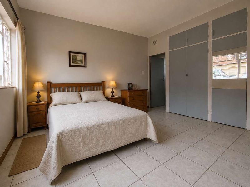 A well-lit bedroom featuring neutral tiled flooring and ample built-in cupboard storage space.