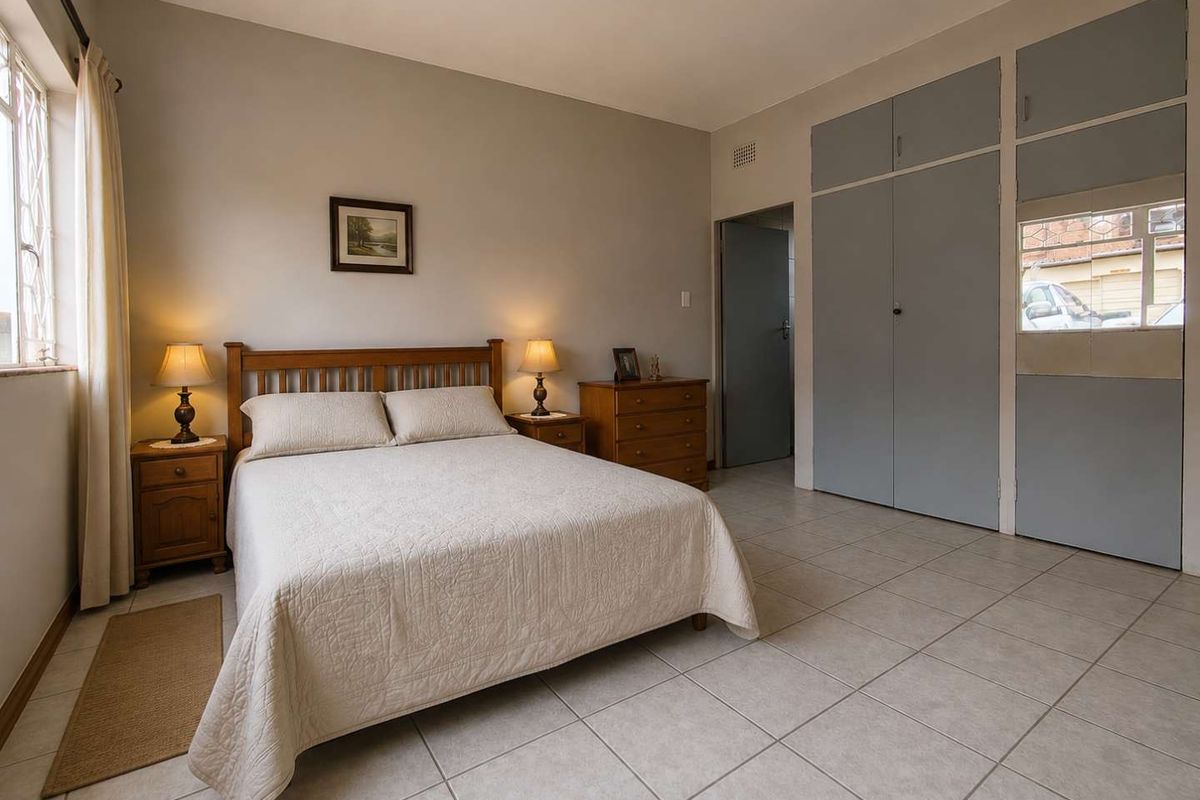 A well-lit bedroom featuring neutral tiled flooring and ample built-in cupboard storage space.