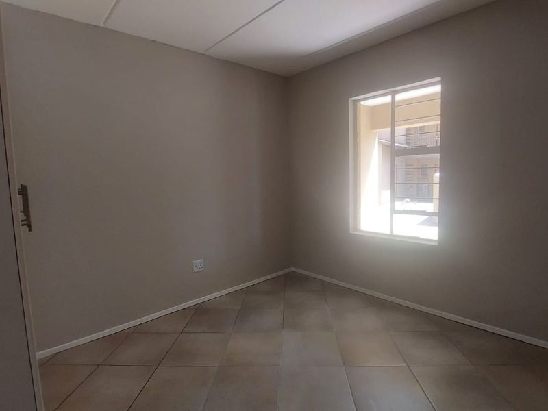 A clean, empty bedroom featuring neutral wall paint, tiled flooring, and a built-in cupboard with security bars on the window.