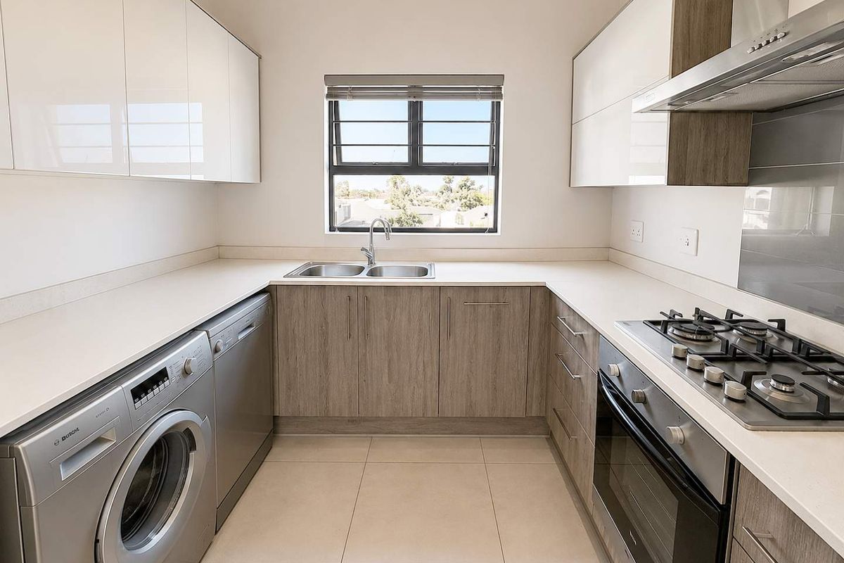 Modern kitchen featuring sleek cabinetry, stone countertops, built-in gas hob, oven, extractor fan, and integrated space for laundry appliances.