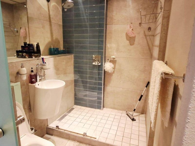 A compact bathroom featuring a walk-in shower with blue accent tiling, a wall-mounted basin, and a toilet.