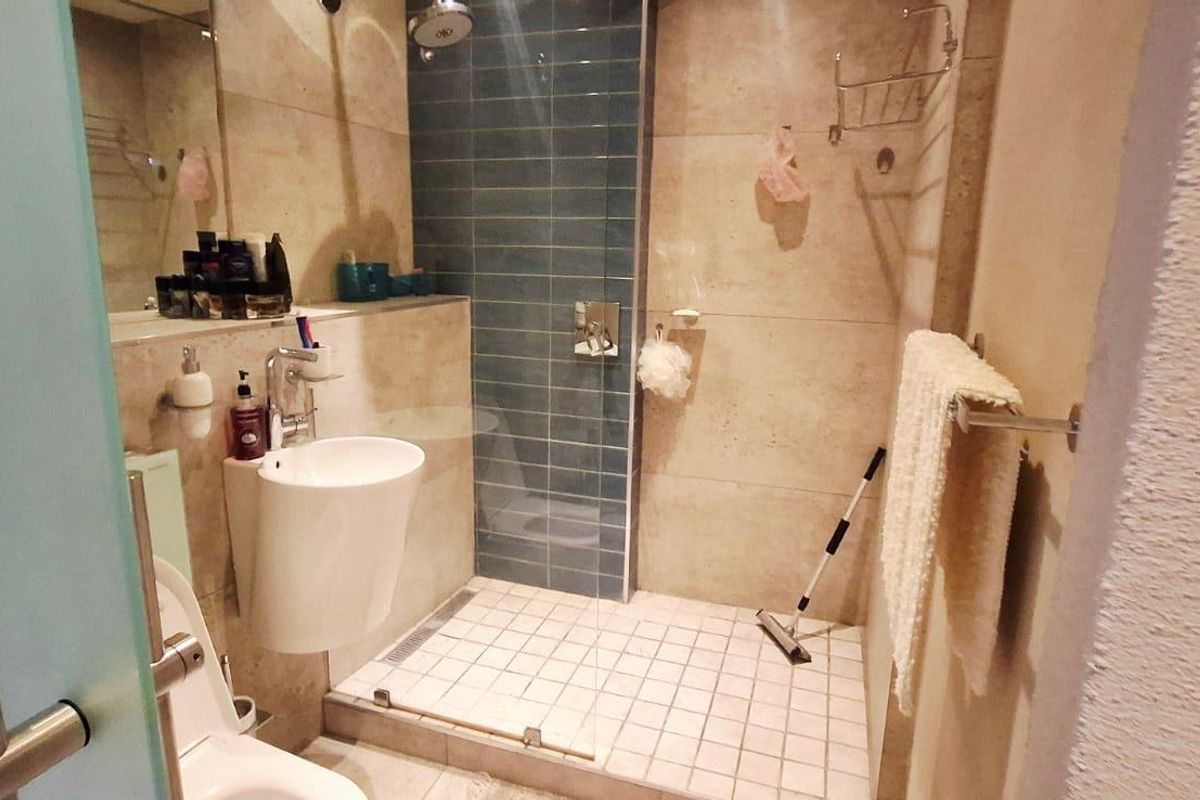 A compact bathroom featuring a walk-in shower with blue accent tiling, a wall-mounted basin, and a toilet.