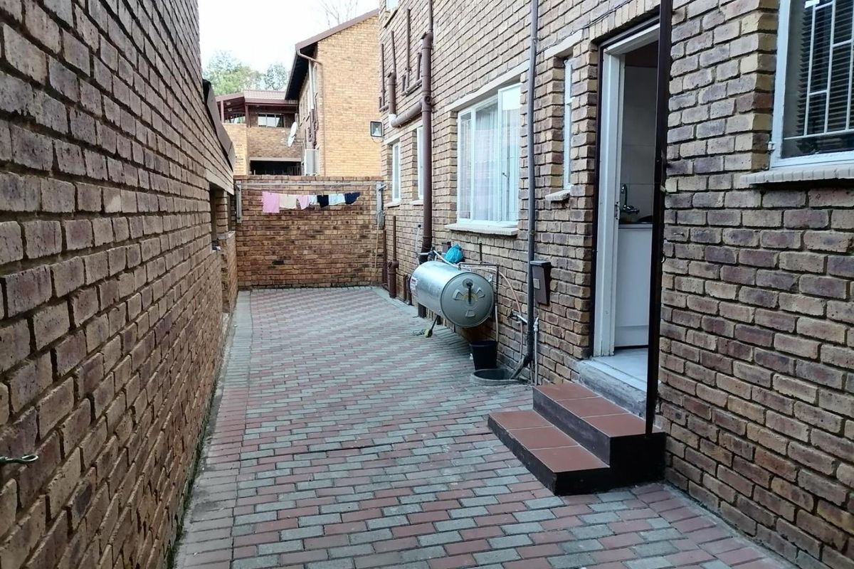 A paved rear courtyard area featuring exposed brick walls, an external geyser unit, and tiled steps leading into the property.