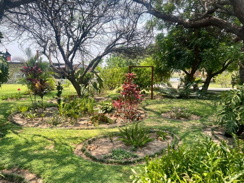 A lush, well-established garden featuring mature trees, manicured garden beds, and a stone wall boundary, offering a serene outdoor environment.
