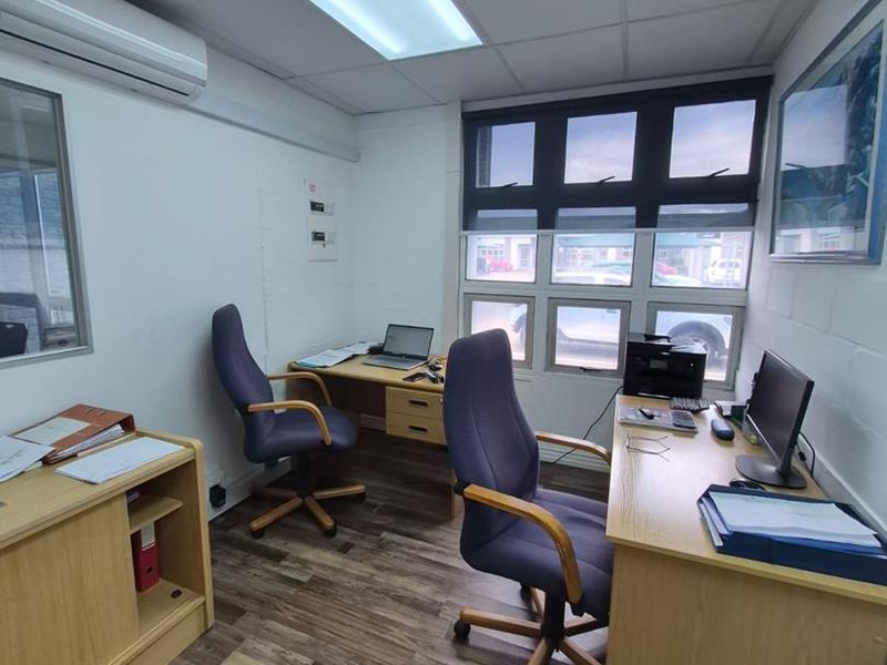 A functional office space featuring laminate wood-look flooring, recessed ceiling lighting, and a wall-mounted split-system air conditioning unit.