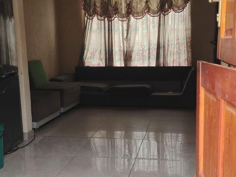 A living room featuring tiled flooring and a timber entrance door, requiring minor cosmetic updates to the ceiling and walls.