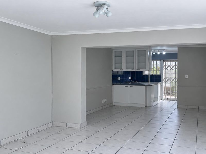 An open-plan living and kitchen area featuring neutral wall tones, tiled flooring, and built-in kitchen cabinetry with a functional layout.