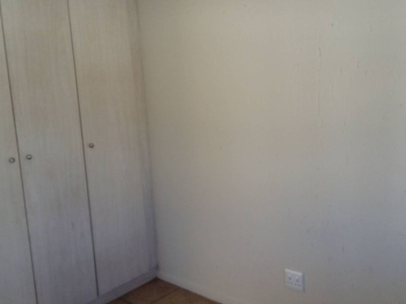 A vacant bedroom featuring built-in cupboards and tiled flooring, requiring minor cosmetic updates to the wall finishes.