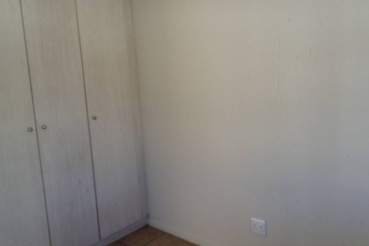 A vacant bedroom featuring built-in cupboards and tiled flooring, requiring minor cosmetic updates to the wall finishes.