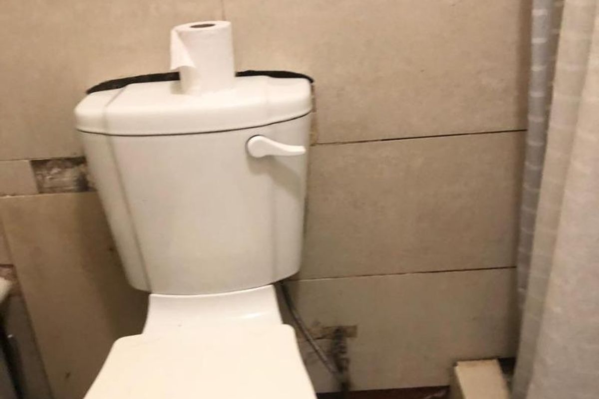 A bathroom featuring a standard toilet and tiled finishes, currently showing signs of wear and unfinished wall sections requiring maintenance or renovation.