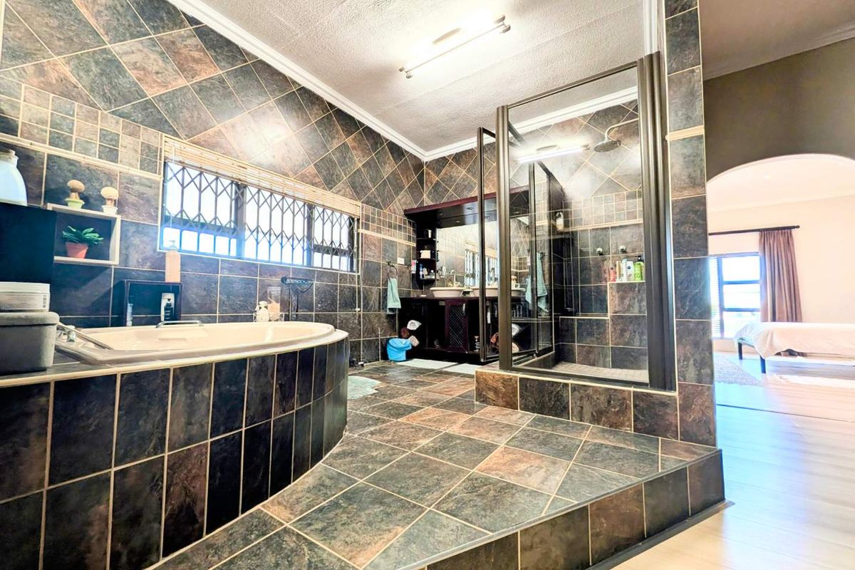Spacious bathroom featuring a raised built-in bathtub, a separate walk-in shower, and a double vanity with dark cabinetry and full-wall tiling.