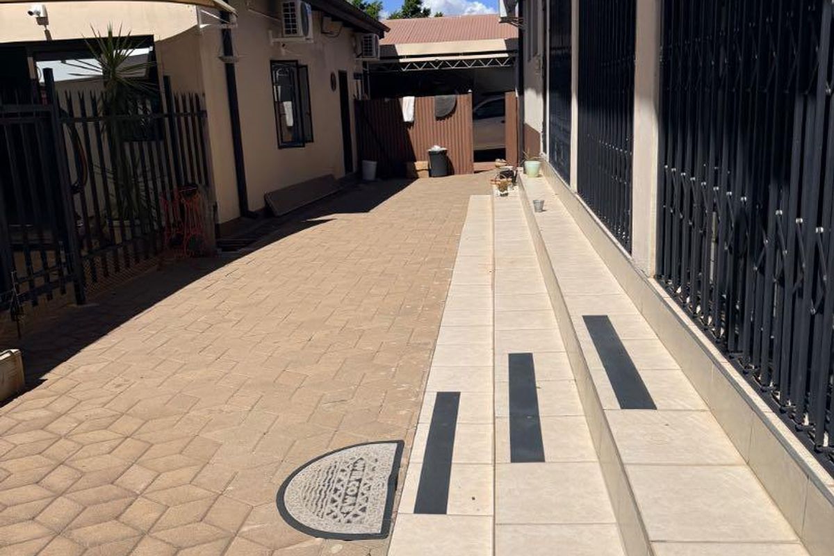 A paved side walkway and patio area featuring tiled steps with safety strips, leading towards the rear of the property.