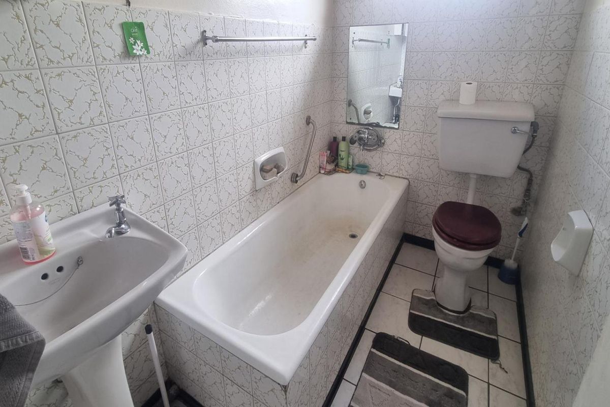 A dated bathroom featuring a pedestal basin, standard bathtub, and toilet with original wall and floor tiling throughout.
