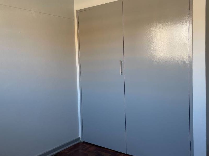 A vacant bedroom featuring classic parquet flooring and built-in cupboards with a neutral grey finish.
