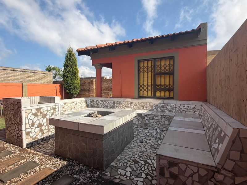 Outdoor patio area featuring a built-in braai, tiled bench seating, and a central fire pit, perfect for entertaining.