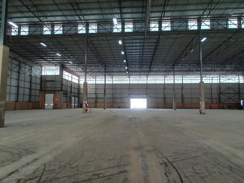 A large, open-plan industrial warehouse space featuring high ceilings, concrete flooring, and extensive natural light through clerestory windows.