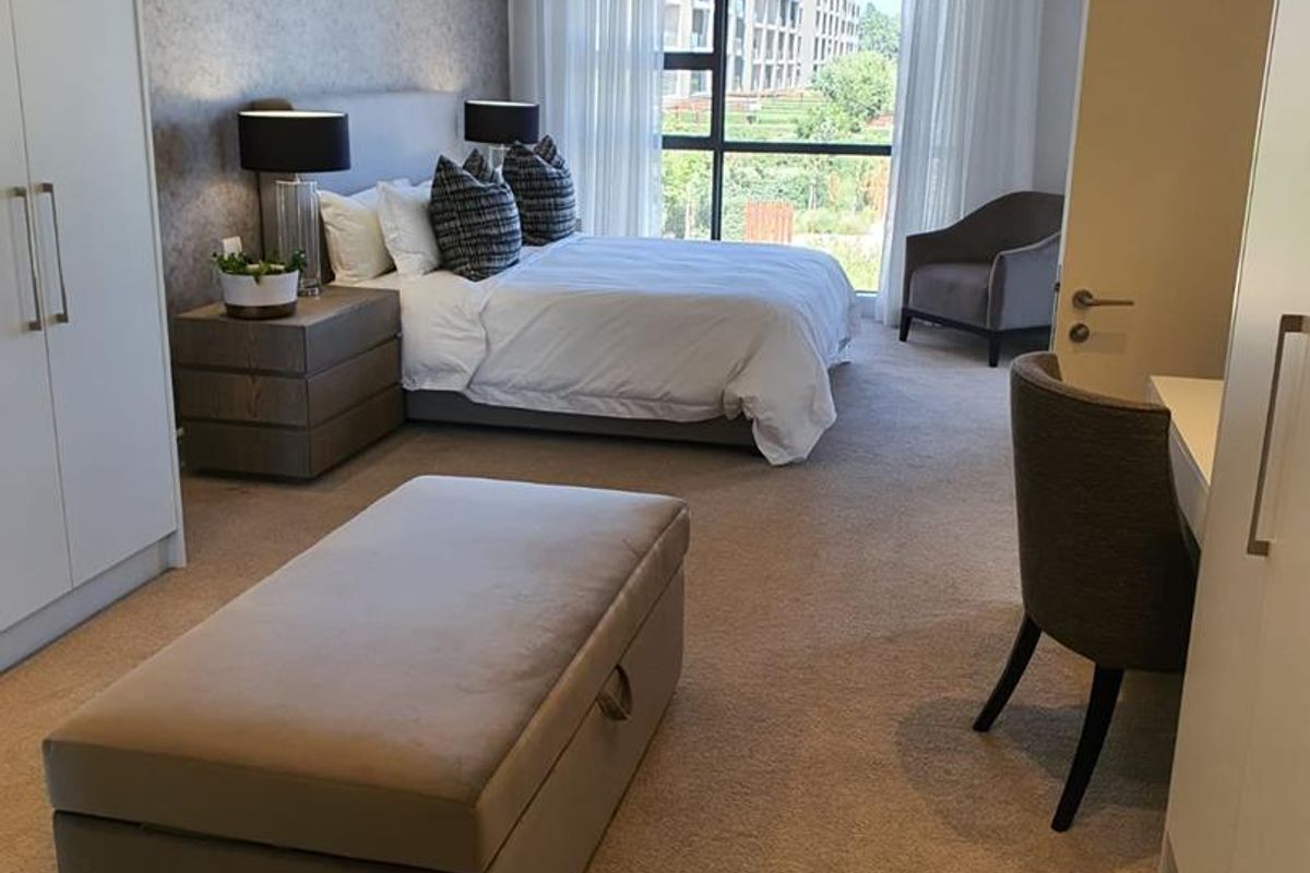 Spacious bedroom featuring built-in wardrobes, recessed ceiling lighting, and large windows providing natural light and views of the surrounding estate.