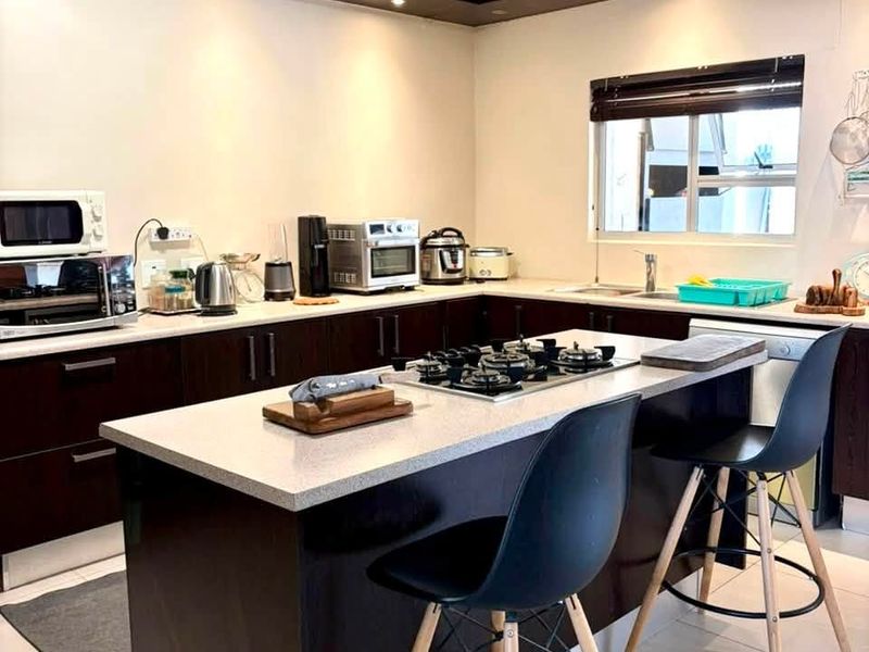Modern kitchen featuring dark wood cabinetry, stone countertops, a central island with a gas hob, and recessed ceiling lighting.