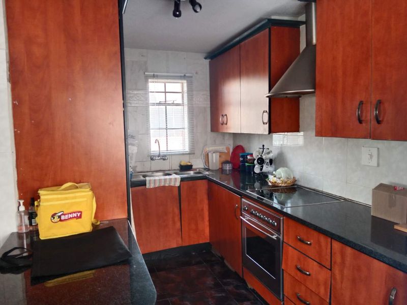 A functional kitchen featuring wood-finish cabinetry, granite countertops, a built-in oven with hob, and a stainless steel extractor fan.