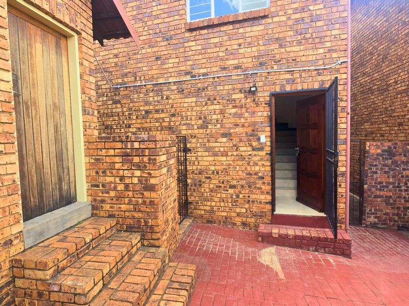 A rear courtyard area featuring face brick walls, paved flooring, and access to the interior via a timber door with a security gate.